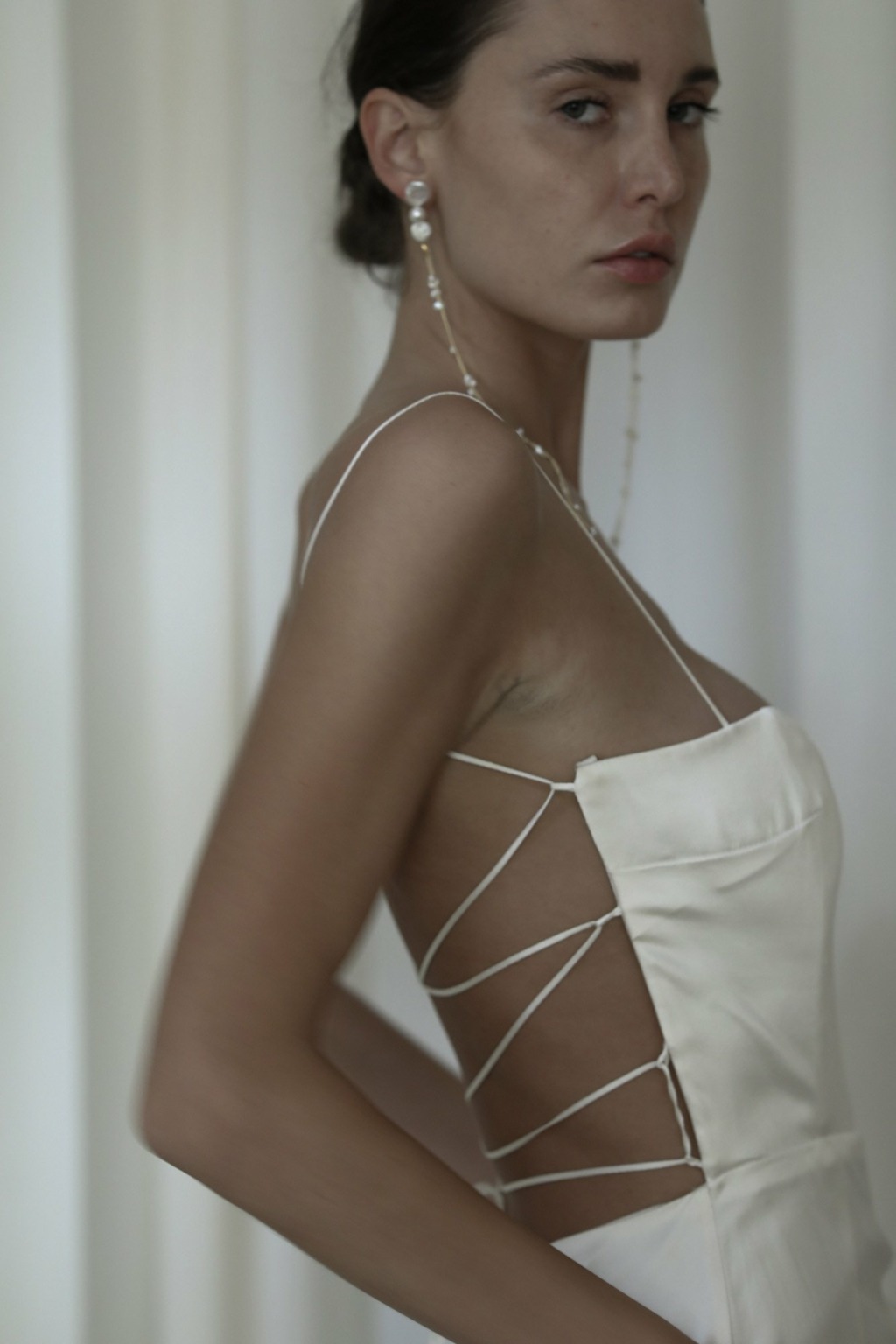 A female model wears pearl strand earrings with a tie-up white dress