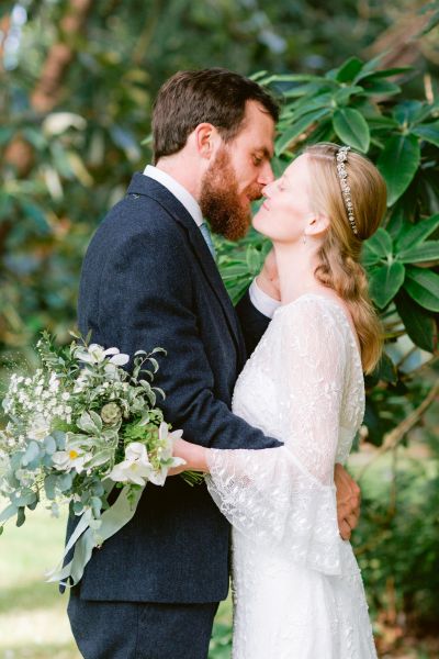 Groom kissing holding bride bouquet flowers exterior