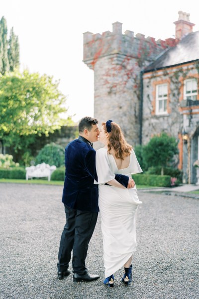 Bride and groom looking over shoulder exterior castle hotel kissing