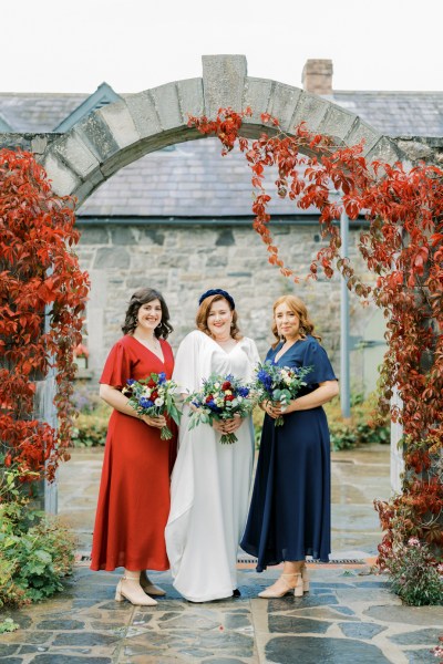 Bride and maid of honour bridesmaid laughing holding bouquet of flowers roses headband red blue dresses exterior