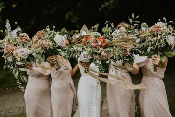 Bride and bridesmaids holding flowers roses in front of faces maid of honour exterior park shot