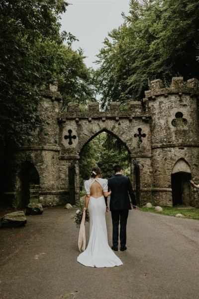 Bride and groom standing before archway castle forest park detail