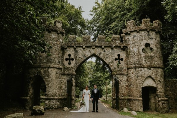 Bride and groom standing before archway castle forest park detail