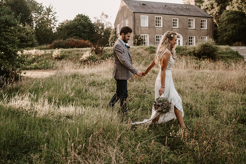 Mark and Lauren's Real Wedding bride and groom photography exterior shot holding hands walking field house