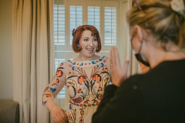 Bride embracing friend hug smiling floral flower dress redhead red hair interior getting ready