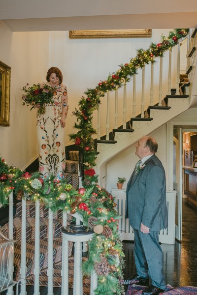 Father of the bride walking down the stairs before ceremony holding bouquet of flowers