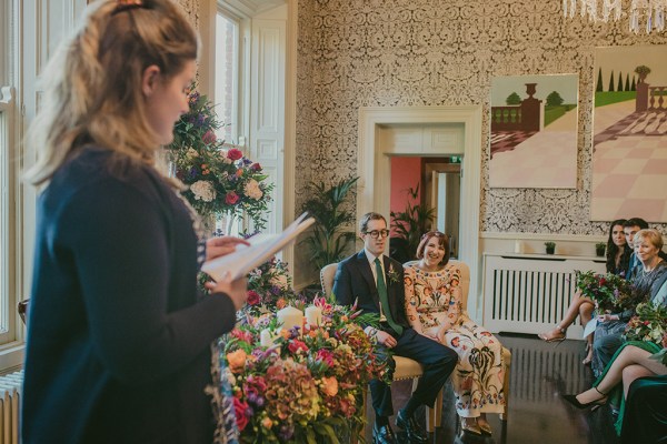 Interior bride and groom floral flowers dress officiant officiate ceremony sitting down guests