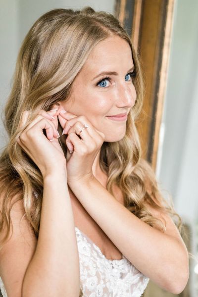 Close up of bride putting earring on jewellery detail lace dress hair blue eyes