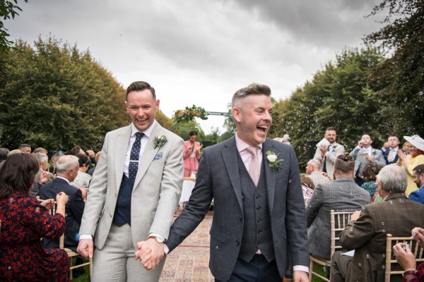 Eoin & Darran Real Wedding grooms hugging couple ceremony exterior congrats bubbles smiling guests clapping