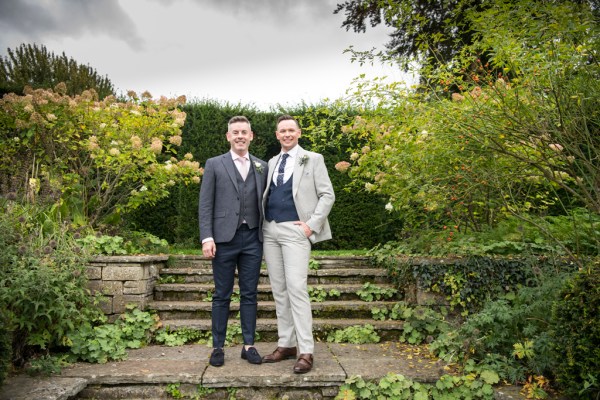 Eoin & Darran Real Wedding grooms smiling to camera suits hand in pocket shoe detail exterior green