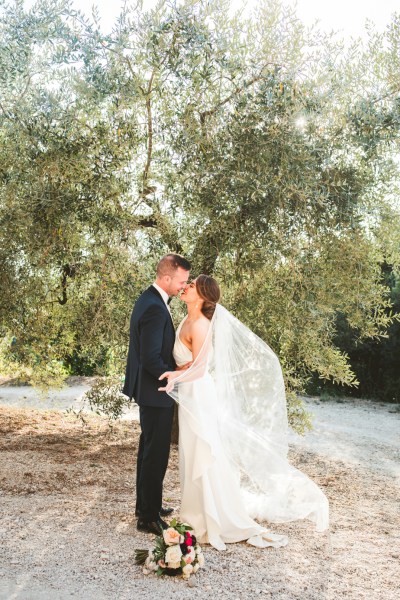 Couple kiss embrace exterior shot bride groom just wed flowers bouquet