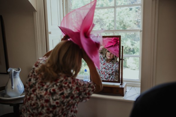 Mother of the bride pink hat floral dress interior getting ready