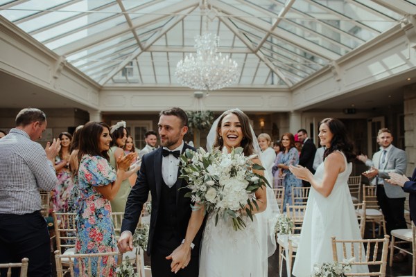 Up close close-up bride groom smiling holding hands happy chandelier guests ceremony