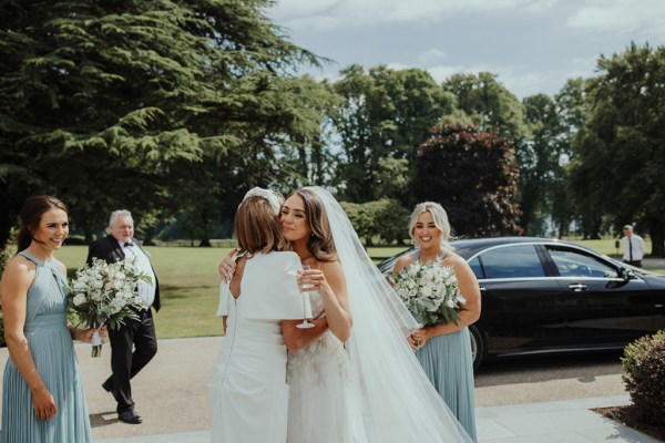 Mother and daughter hug bride embrace bridesmaids car exterior