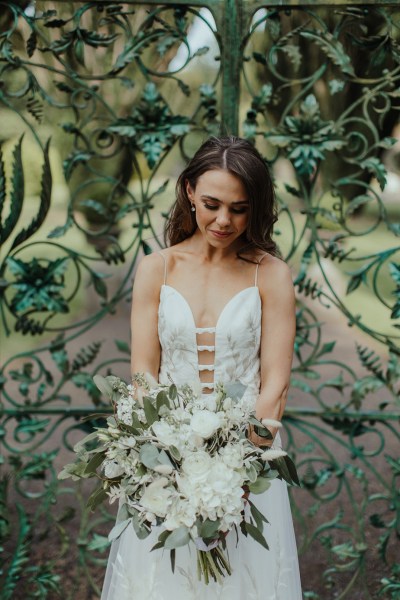 Bride holding bouquets of flowers looking down gate exterior