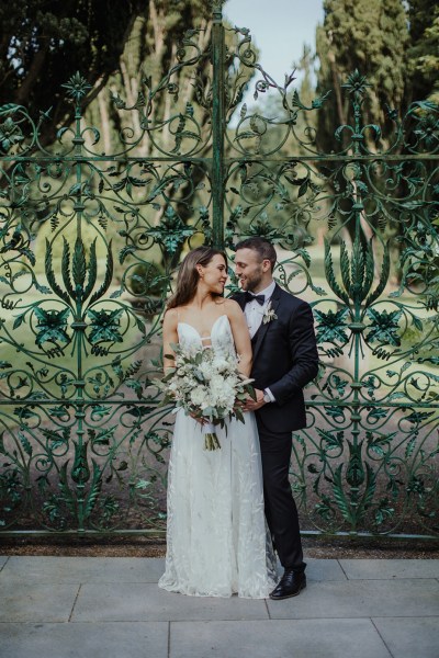 Couple photography exterior gate hold embrace bouquet of flowers looking at each other