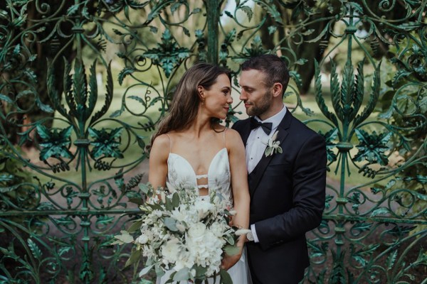 Couple photography exterior gate hold embrace bouquet of flowers looking at each other