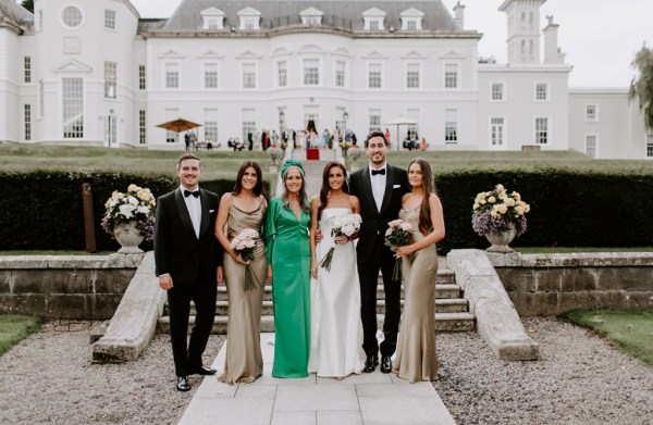 Family shot bridesmaid groom bride man and wife steps exterior hotel green dress satin