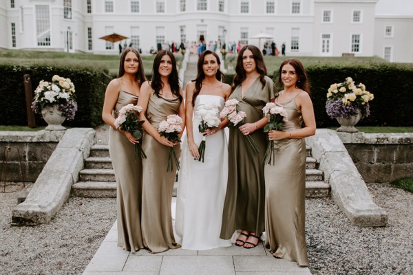 Bride holding white roses flowers with bridesmaids maid of honour bouquet steps exterior hotel shot