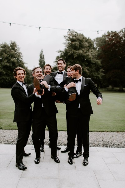 Groomsmen carrying groom best man exterior shot black suits tie