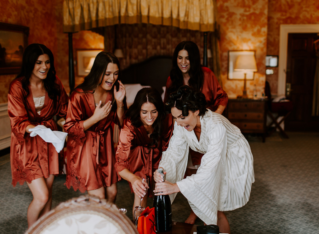 Bridesmaids wearing satin gowns before ceremony wedding bride opening champagne prosecco glasses laughing