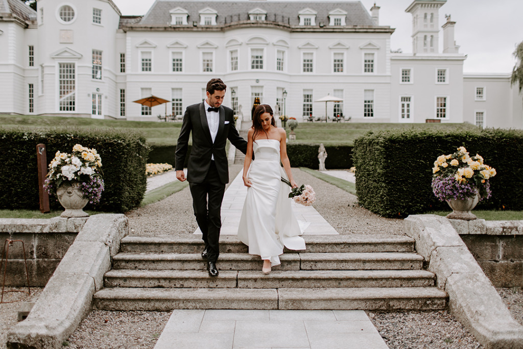 Exterior bride and groom walking down hotel steps flowers holding pink roses bouquet