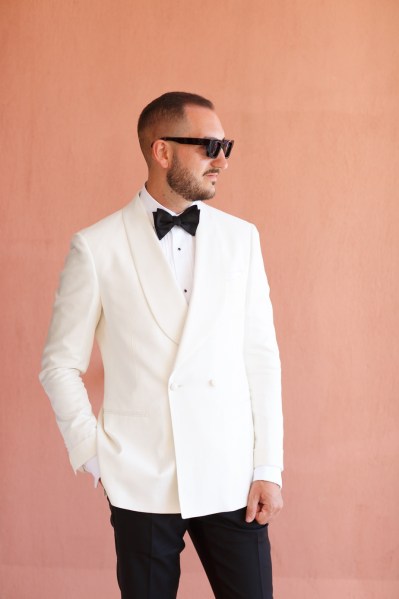 Orange background of groom white suit black tie wearing glasses