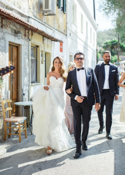 Bride walking groomsmen bridesmaids exterior cafe holding dress friends family