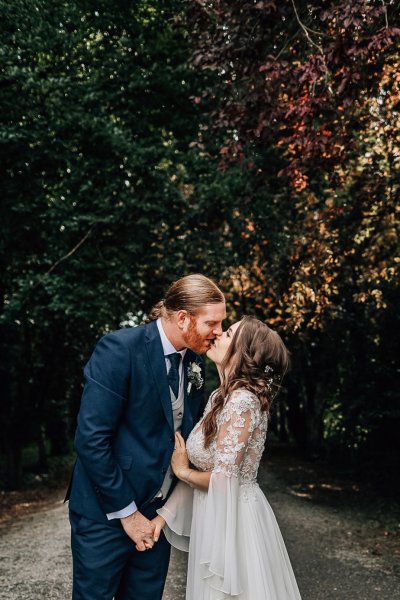 Bride and groom kiss forest autumn colour trees in background