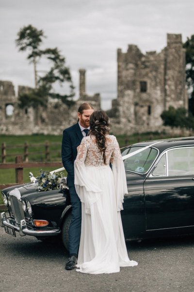 Bride and groom against wedding car castle in background