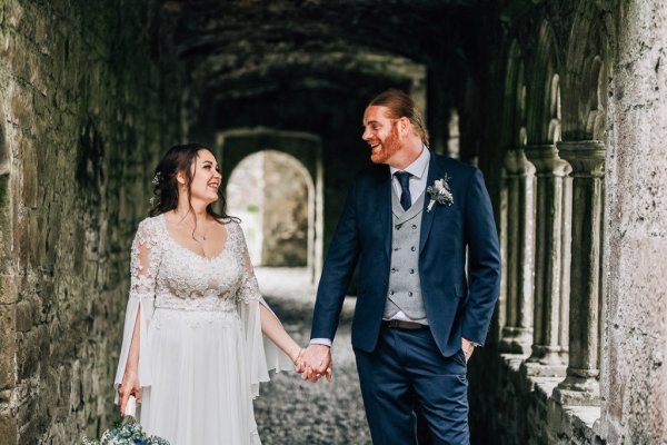 Bride and groom walking under bricked castle exterior