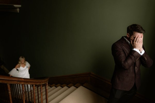 Groom covering face as bride walks up the stairs