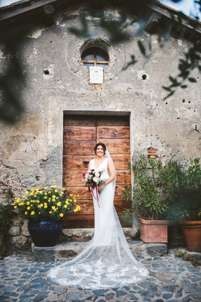 bride with bridal bouquet with red pink flowers and horseshoe charm wearing cathedral veil