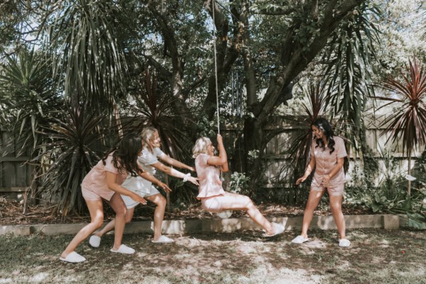 Bride on swing with bridesmaids having fun in silk pyjamas