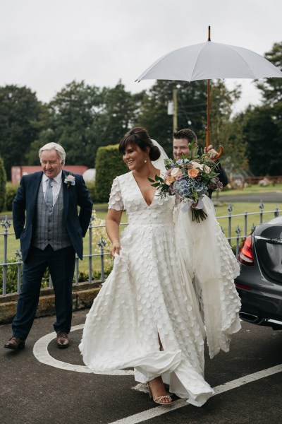 Bride under umbrella raining exterior wedding car family