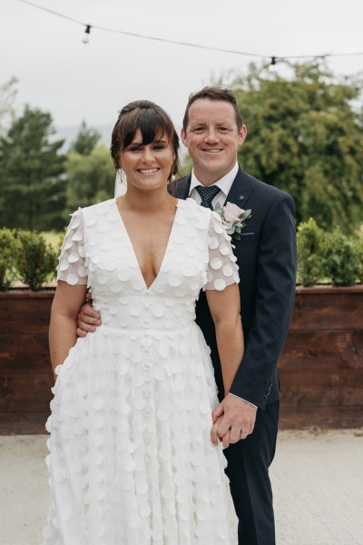 Bride and groom look to camera exterior shot dress detail suit pink rose