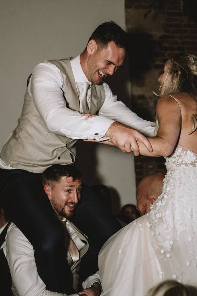 bride and groom on guests shoulders