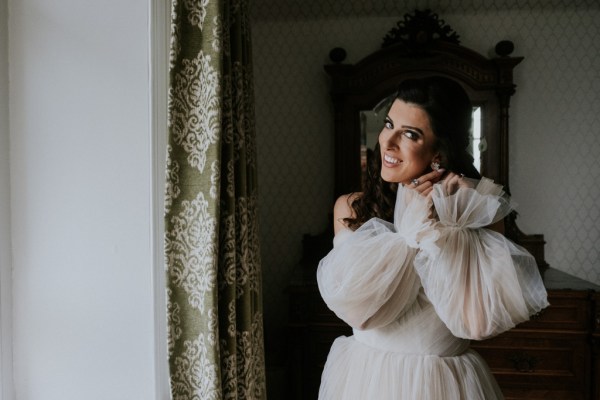 Bride puts on her earrings in mirror reflection