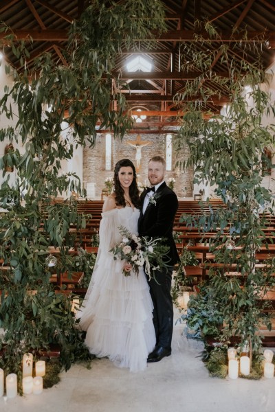 Bride and groom stand surrounded by flower bed pews in background