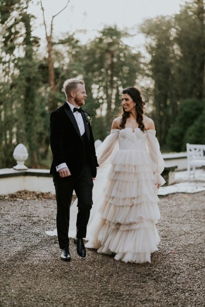 Bride and groom walk in forest setting hand in hand walking towards venue