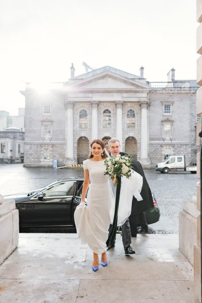 Father of the bride walking into church holding bouquet of flowers