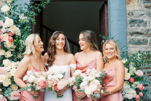 bride with peach bridesmaids outside church floral pillars