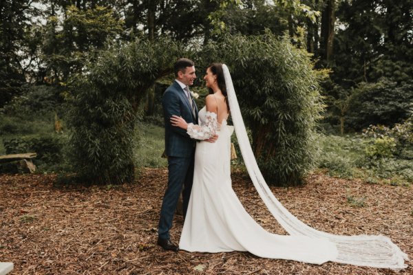 Bride groom laughing looking at each other flowers dress train veil