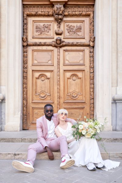 Groom bride sitting against wooden door bouquet flowers