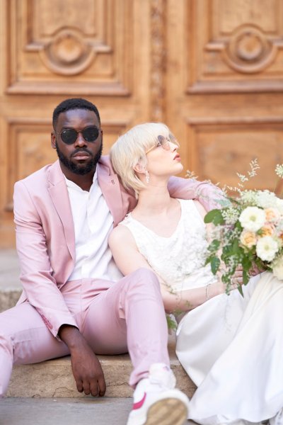 Groom bride sitting against wooden door bouquet flowers