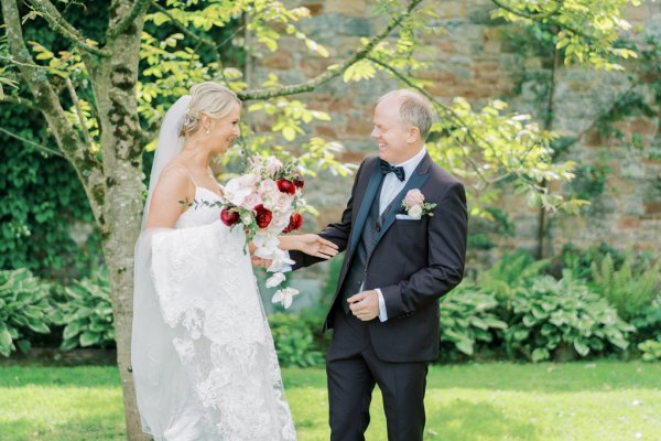 first look Bride holding roses pink red and groom in garden