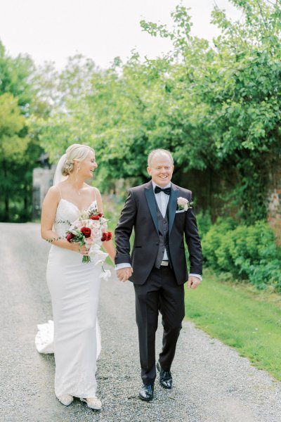 Bride holding roses pink red and groom in garden walking