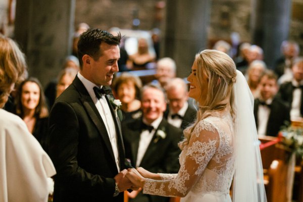 Bride groom alter church guests priest holding hands