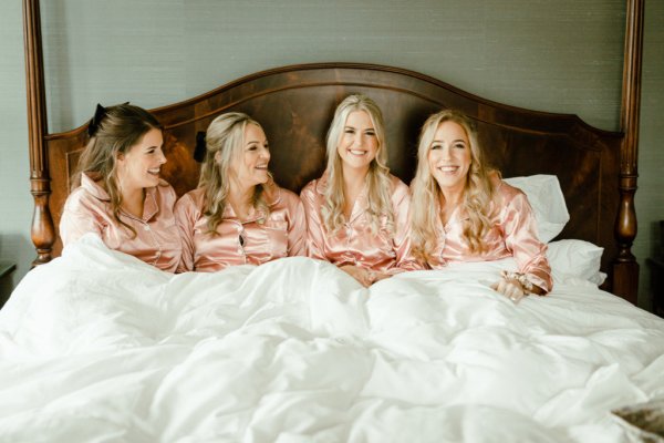 Bride in pink satin pajamas loungewear with bridesmaids in bed