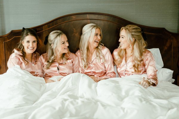 Bride in pink satin pajamas loungewear with bridesmaids in bed